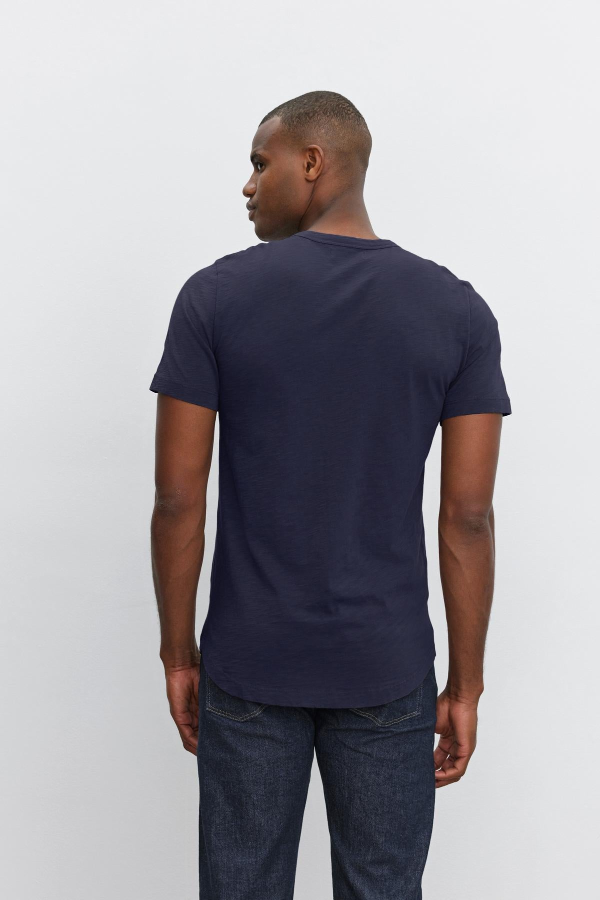   Man wearing a dark blue Velvet by Graham & Spencer crew neck AMARO TEE with heathered texture and denim jeans standing against a white background, viewed from behind. 