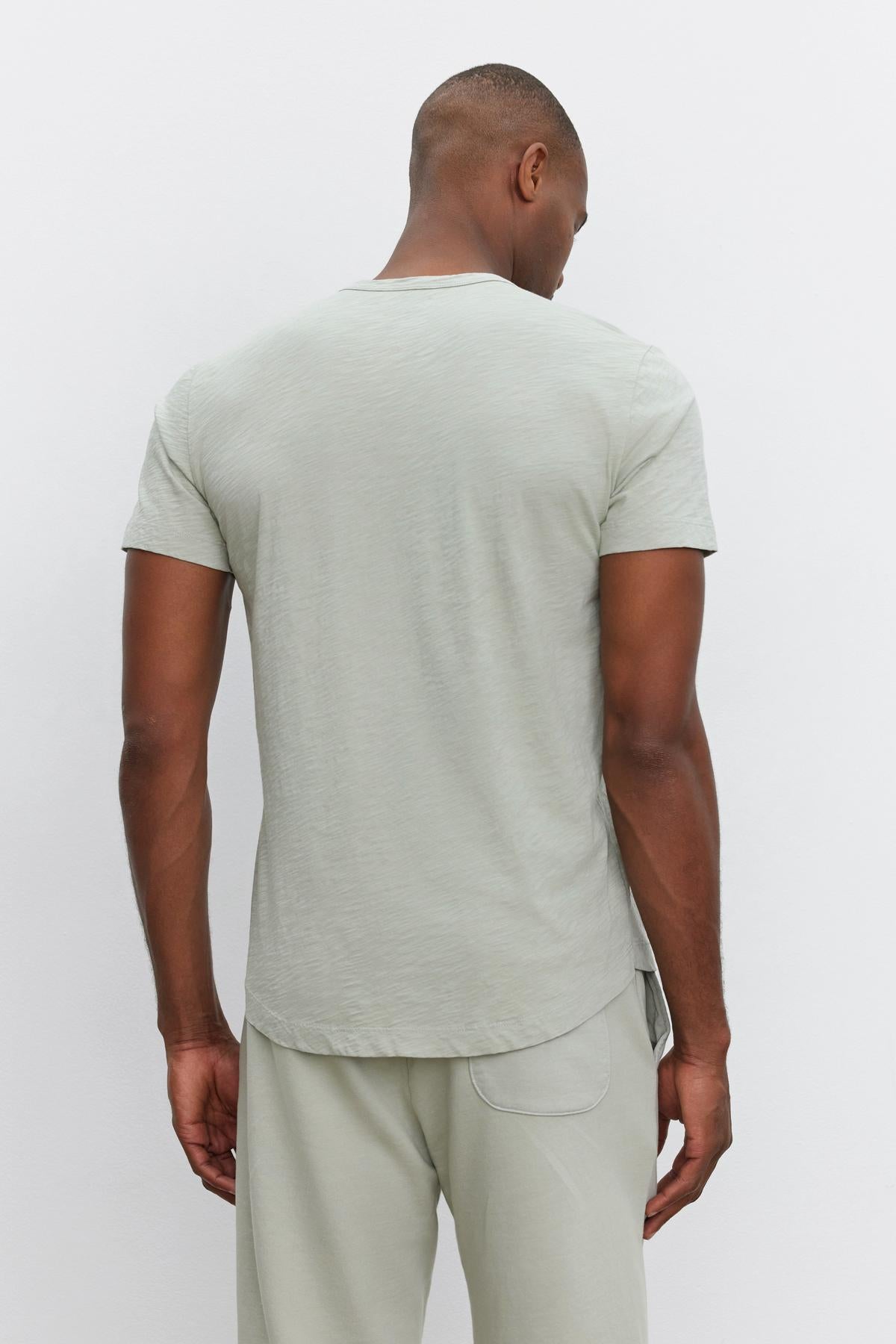   A person stands facing away, wearing a light gray short-sleeve AMARO TEE by Velvet by Graham & Spencer and matching pants, exuding a relaxed and stylish feel. 