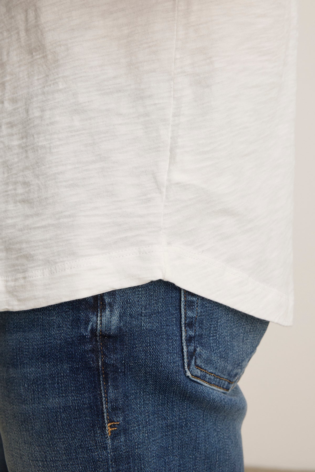   Close-up of a person wearing the AMARO TEE by Velvet by Graham & Spencer, made from soft Peruvian cotton, paired with blue jeans showing the side and back pocket details. 