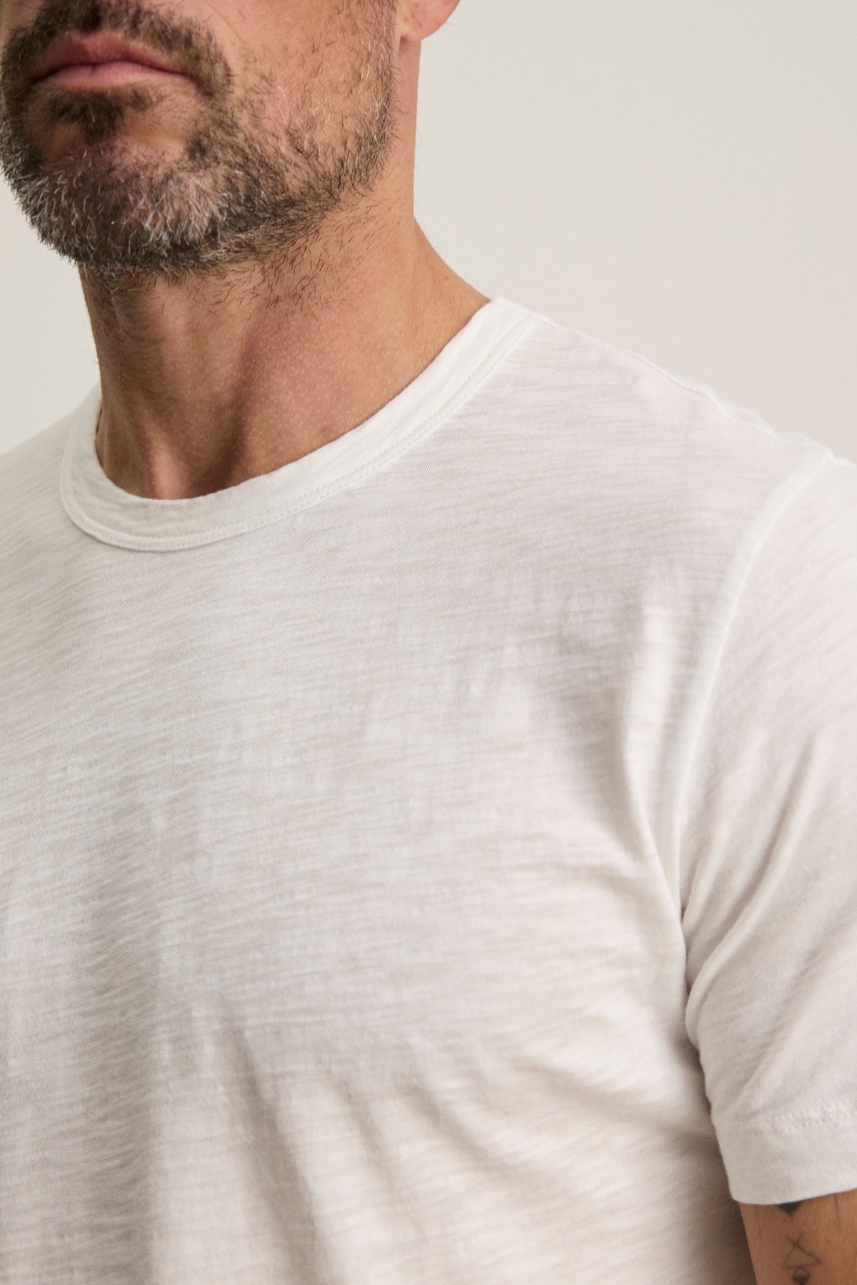 A bearded person wears the AMARO TEE by Velvet by Graham & Spencer, a plain white T-shirt made from soft Peruvian cotton with a classic crew neckline—perfect for versatile layering.-38504000848065