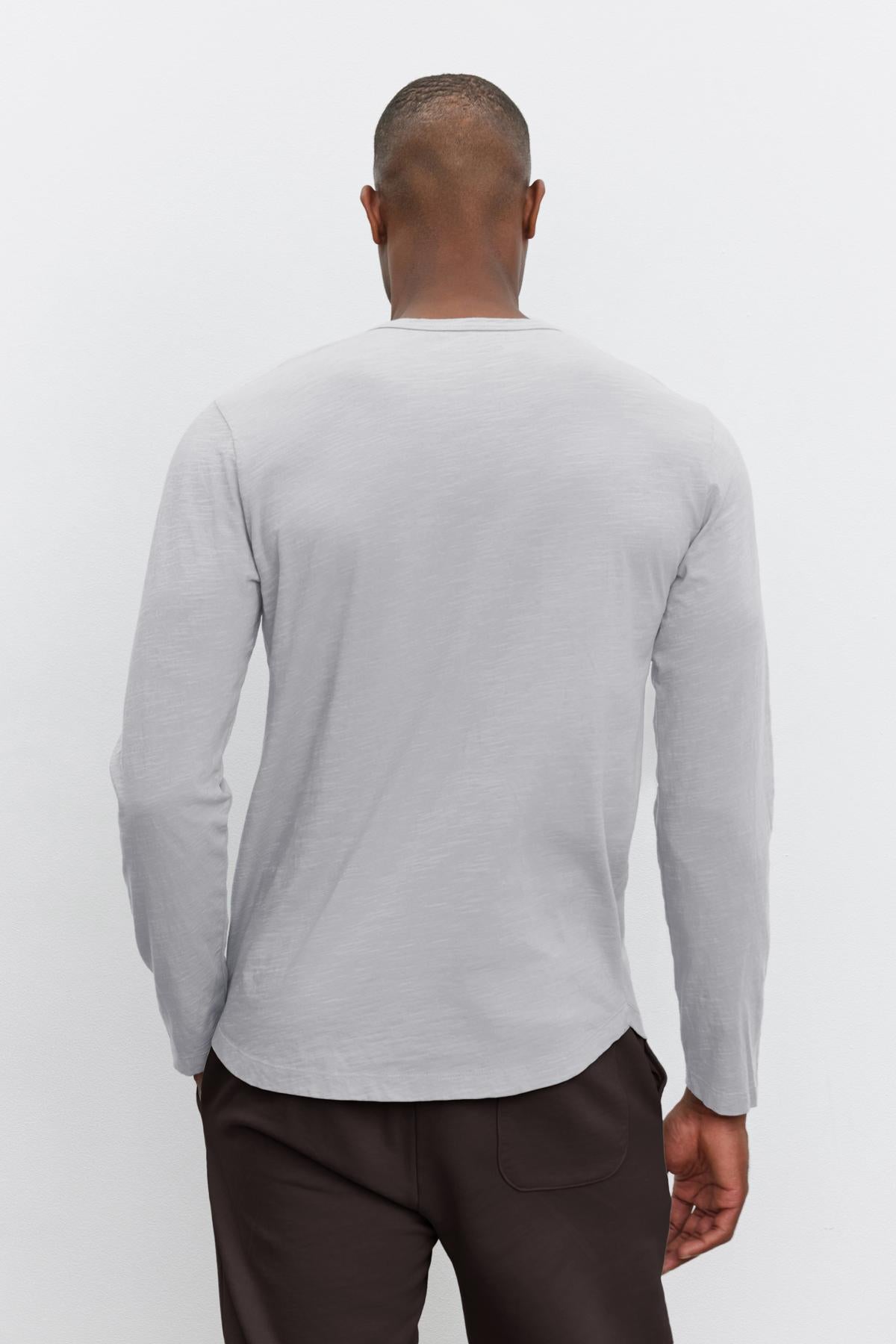 An individual wearing the KAI TEE in gray, designed by Velvet by Graham & Spencer, paired with dark pants is photographed from behind against a plain background, highlighting its timeless design.-38264831639745