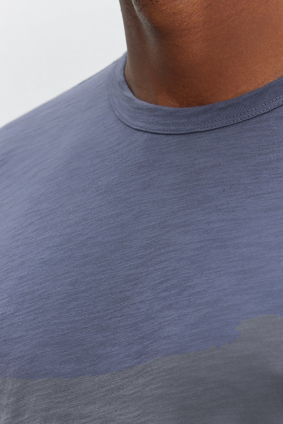   Close-up of a person wearing the KAI TEE, a blue crew neck t-shirt made from Peruvian cotton by Velvet by Graham & Spencer. Only the lower half of their face and the upper torso are visible, showcasing the timeless design and classic crew neckline. 