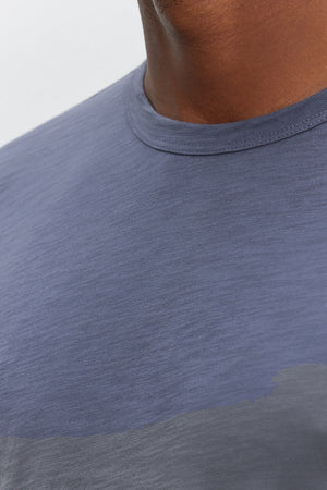 Close-up of a person wearing the KAI TEE, a blue crew neck t-shirt made from Peruvian cotton by Velvet by Graham & Spencer. Only the lower half of their face and the upper torso are visible, showcasing the timeless design and classic crew neckline.