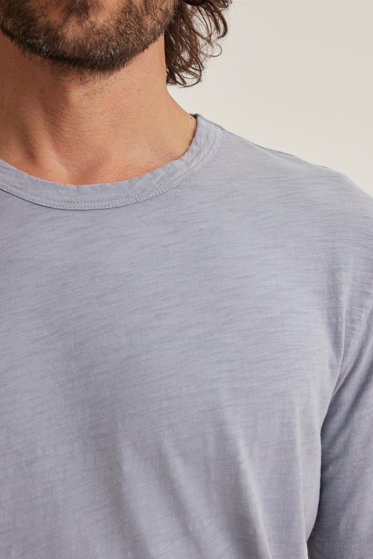 A man wearing the KAI TEE by Velvet by Graham & Spencer, a light gray T-shirt with a classic crew neckline, displays part of his face and medium-length hair. Crafted from luxurious Peruvian cotton, it embodies timeless design that enhances his casual yet sophisticated look.-38643308527809