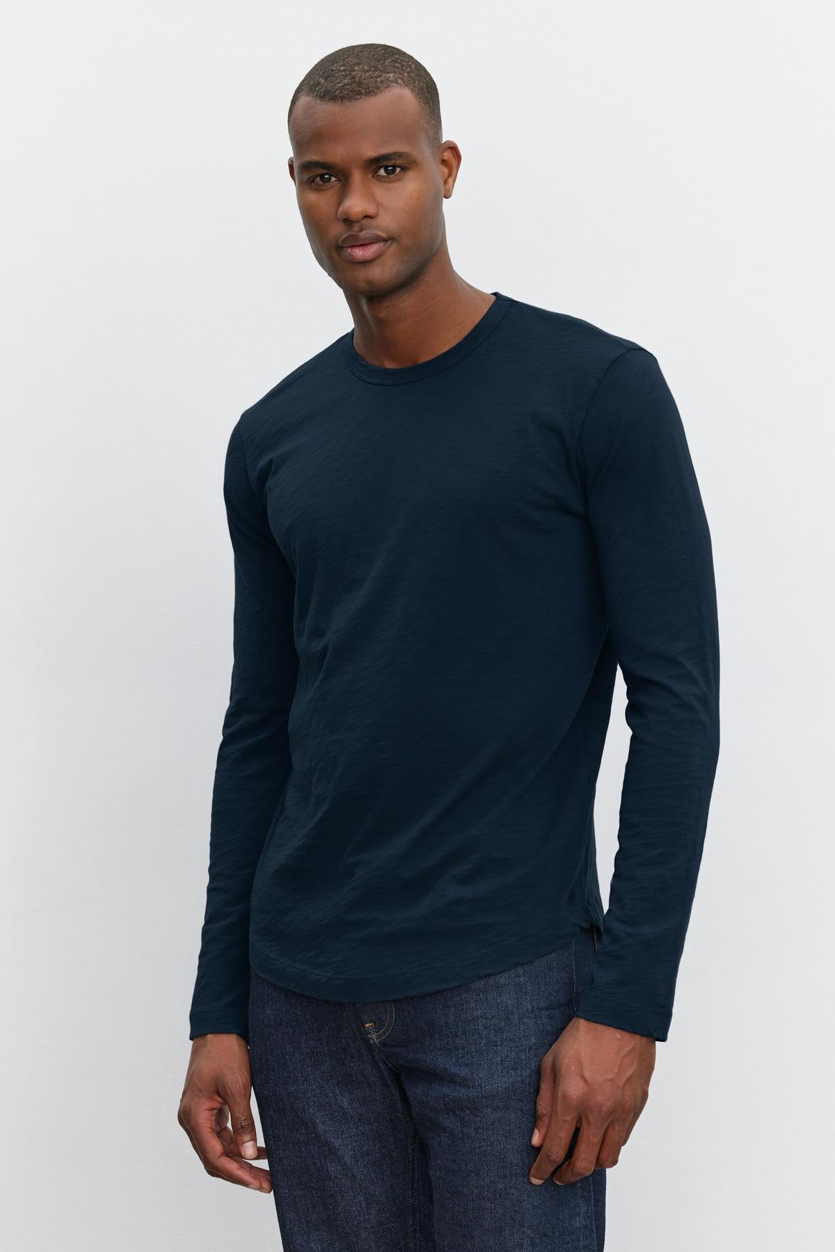   A person wearing a navy blue KAI TEE by Velvet by Graham & Spencer with a classic crew neckline and dark blue jeans stands against a plain white background. 