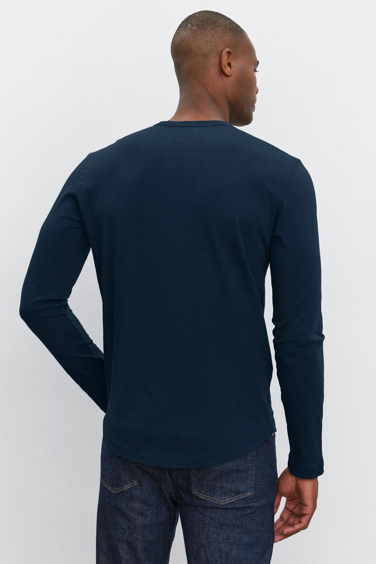 A person is shown from behind wearing a long-sleeve, dark blue KAI TEE by Velvet by Graham & Spencer with a classic crew neckline and dark denim jeans.-37469162373313