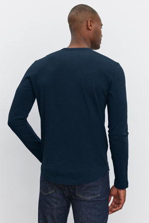 A person is shown from behind wearing a long-sleeve, dark blue KAI TEE by Velvet by Graham & Spencer with a classic crew neckline and dark denim jeans.