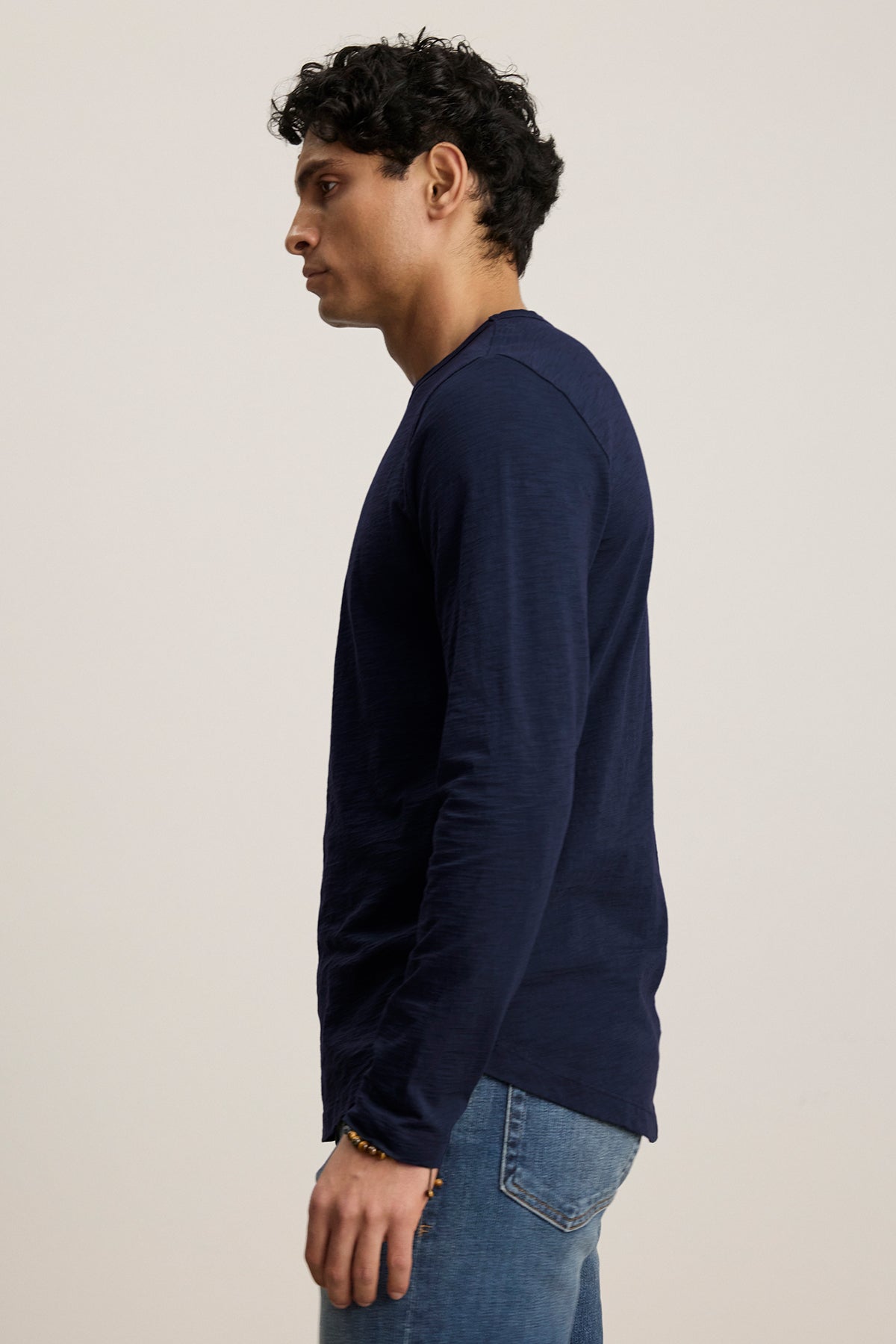 A person in a Velvet by Graham & Spencer KAI TEE, featuring classic navy long sleeves and paired with jeans, poses sideways against a plain background to highlight its timeless design.-38807449305281