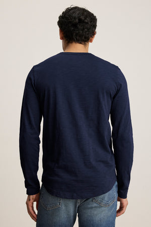 A man with curly hair, wearing the KAI TEE by Velvet by Graham & Spencer in navy, crafted from luxurious Peruvian cotton with a classic crew neckline, paired with jeans, faces away from the camera.