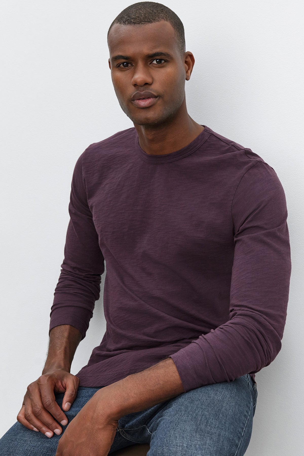 A person wearing the long-sleeve KAI TEE shirt by Velvet by Graham & Spencer, made from Peruvian cotton, and blue jeans sits against a plain white background.-37893903319233