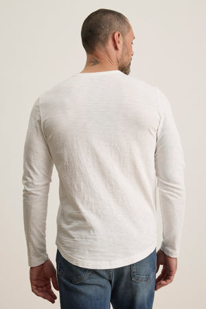 A man wearing Velvet by Graham & Spencer's KAI TEE, a white long-sleeve shirt made from luxurious Peruvian cotton with a classic crew neckline, turns away, showcasing a small neck tattoo.