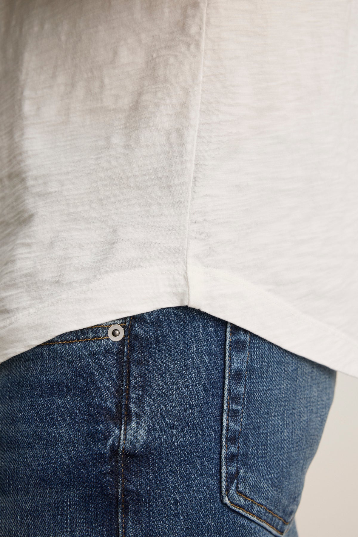 Close-up of a person wearing the KAI TEE by Velvet by Graham & Spencer, featuring a white classic crew neckline and blue jeans, highlighting the textures and stitches of its Peruvian cotton fabric.-38504007237825