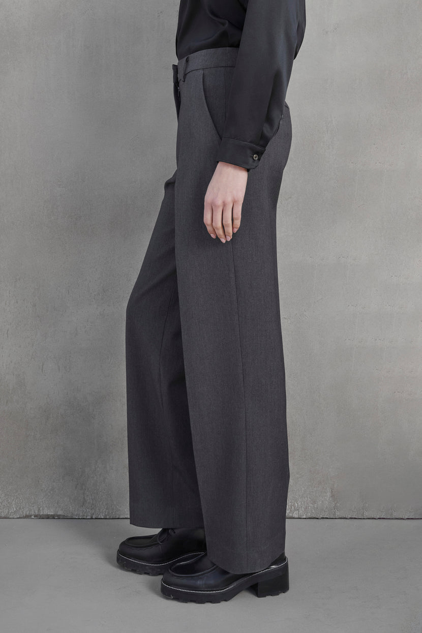 A person standing against a gray background, wearing the high-waisted, wide-leg PRINCE PANT in suiting fabric with pleats from Velvet by Jenny Graham and black shoes.