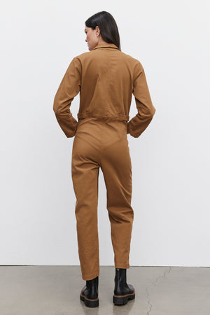 Individual wearing the Velvet by Graham & Spencer BRINLEY JUMPSUIT in brown stretch cotton twill and black boots, standing with their back turned to the camera.