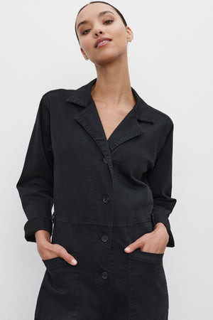 A person is standing against a plain background, wearing the BRINLEY JUMPSUIT from Velvet by Graham & Spencer with their hands in their pockets.