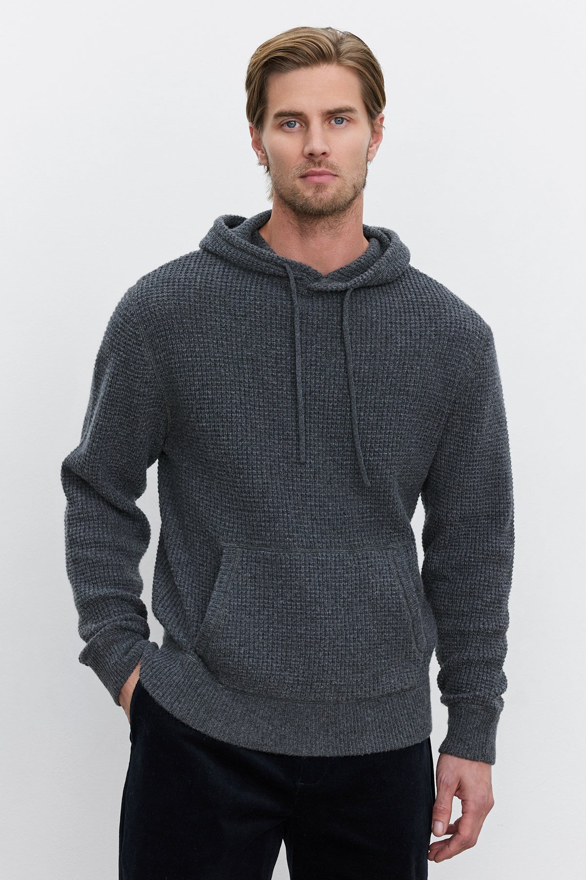 A man with light brown hair and a beard wearing the SHANE SWEATER HOODIE by Velvet by Graham & Spencer and black pants stands against a plain white background.-37893929795777