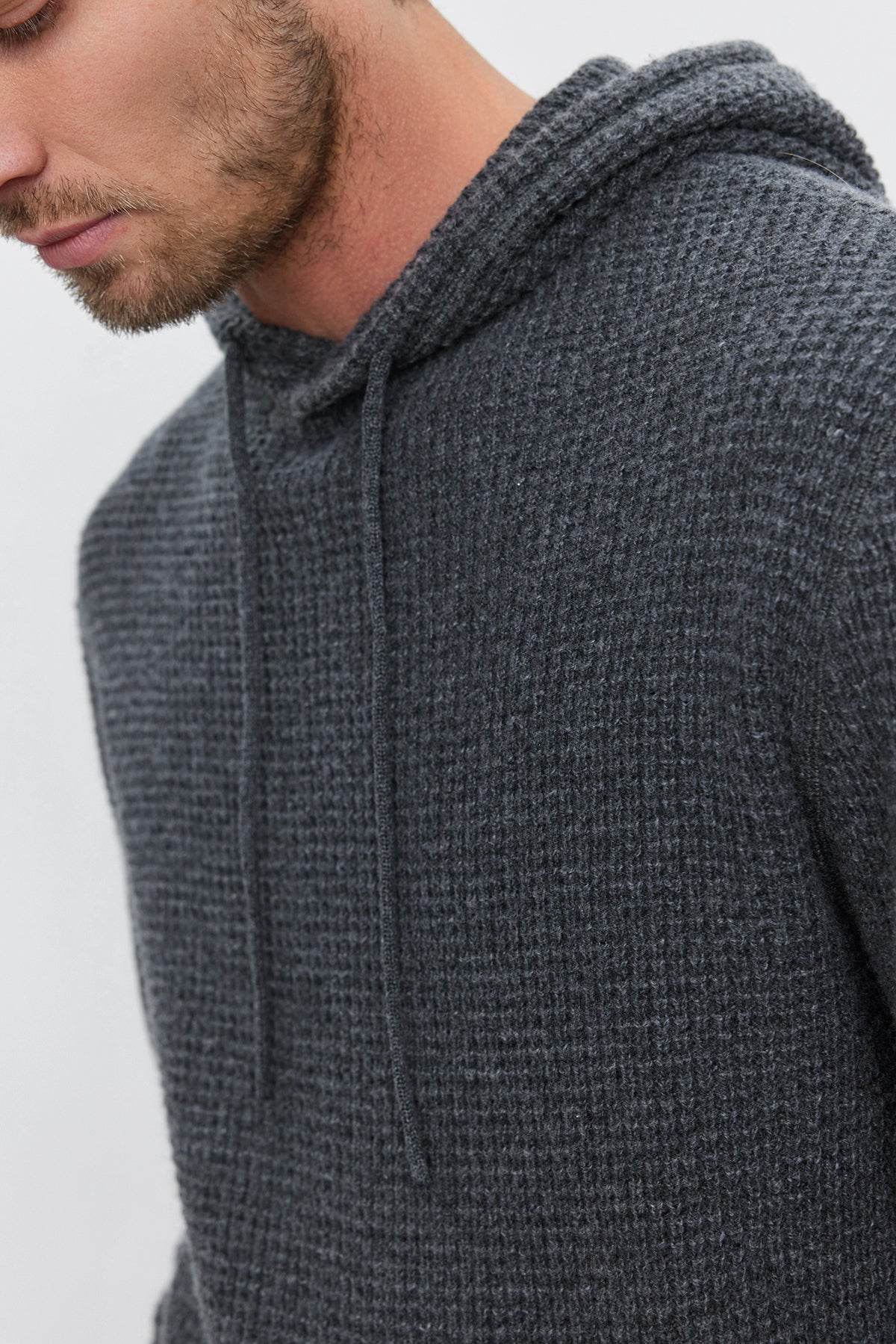   A man wearing a SHANE SWEATER HOODIE by Velvet by Graham & Spencer, in textured gray with visible drawstrings, photographed from the shoulders up, exuding warmth and comfort. 