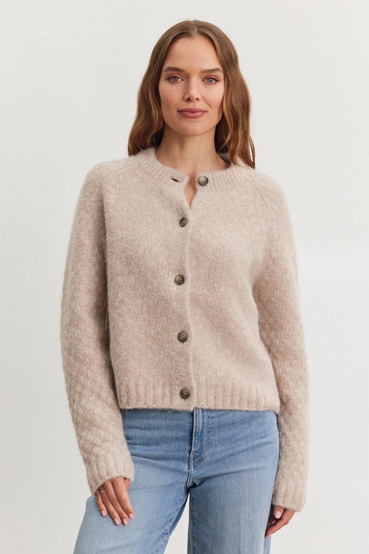 A person wearing the CHANTAL ALPACA CARDIGAN from Velvet by Graham & Spencer, featuring a beige alpaca-blend with a five-button front and ribbed trims, paired with blue jeans, stands against a plain backdrop.-38301315367105