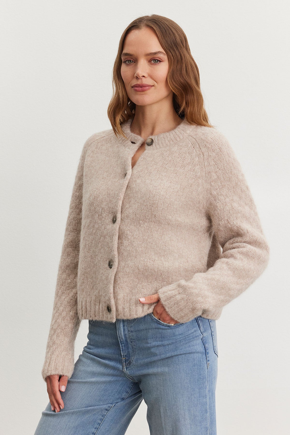   A person stands wearing the CHANTAL ALPACA CARDIGAN by Velvet by Graham & Spencer, layered over a textured sweater and paired with blue jeans against a plain background. 