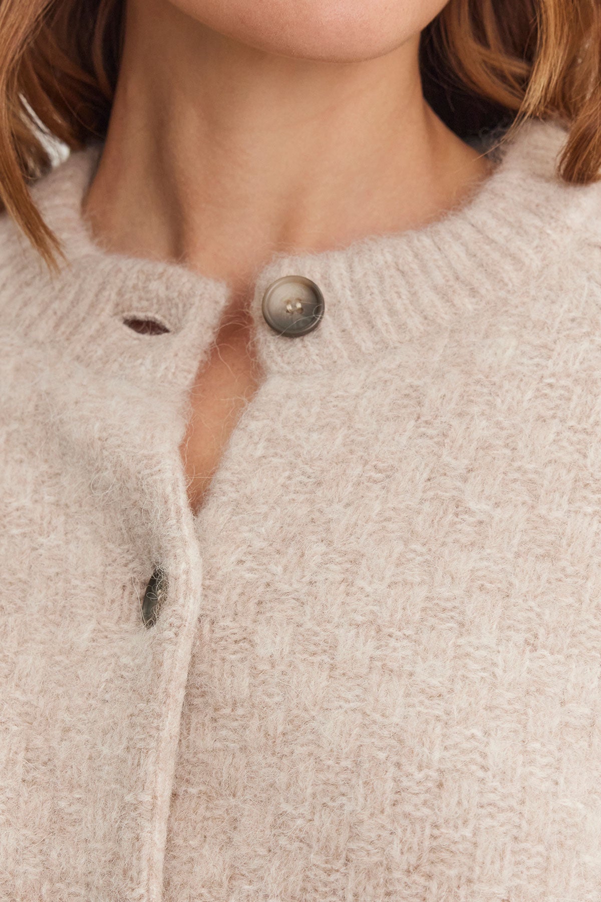   A close-up of an individual wearing the CHANTAL ALPACA CARDIGAN in a light beige hue, designed by Velvet by Graham & Spencer, showcasing ribbed trims and a five-button front. 