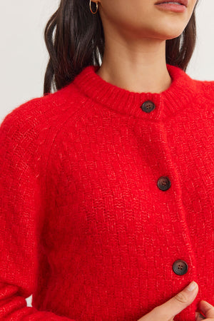 A person wearing the CHANTAL ALPACA CARDIGAN by Velvet by Graham & Spencer, crafted from a vibrant red alpaca blend and embellished with large buttons.