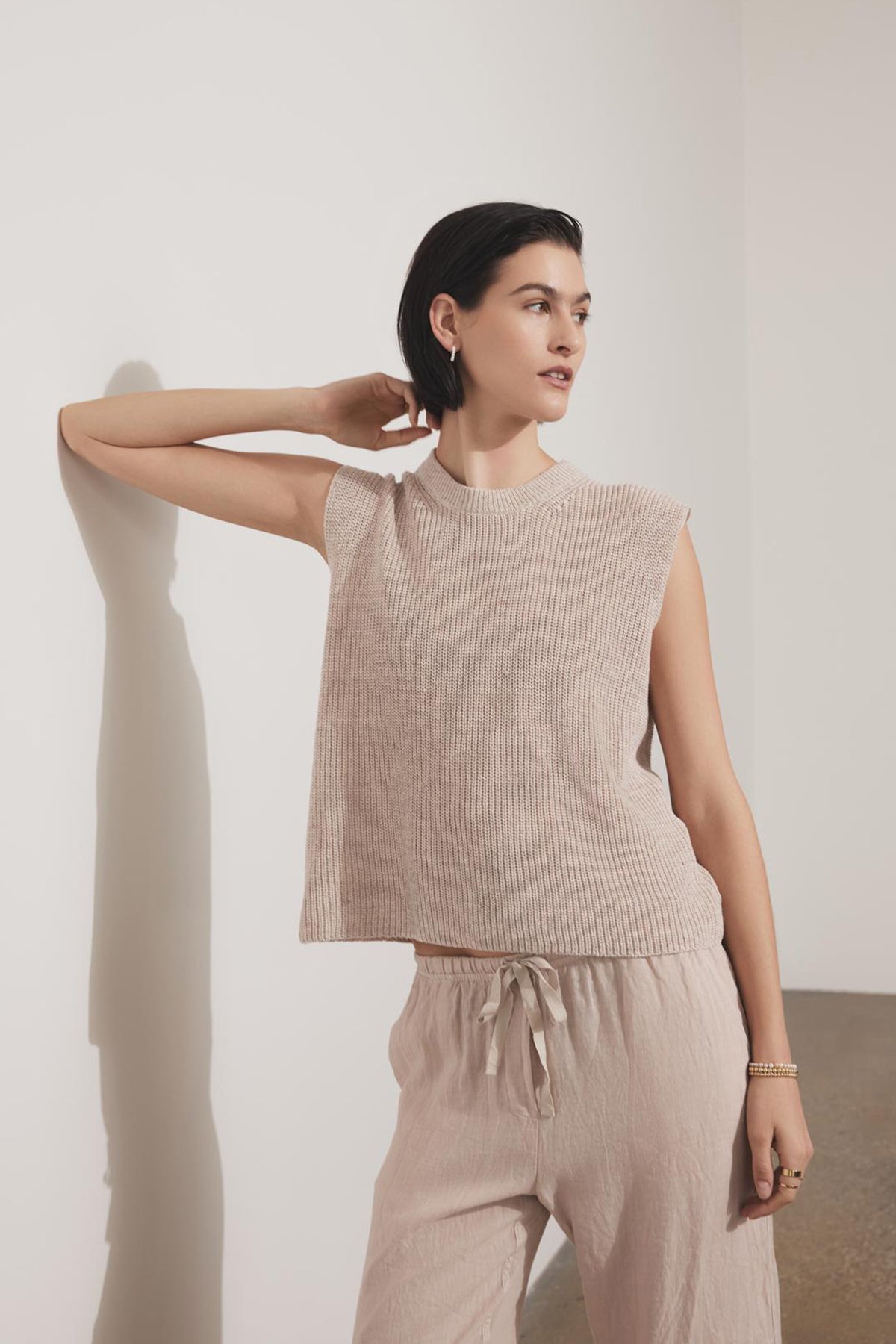   Woman in a GARDENA LINEN SWEATER VEST by Velvet by Jenny Graham and matching pants posing with one hand behind her head against a plain background. 