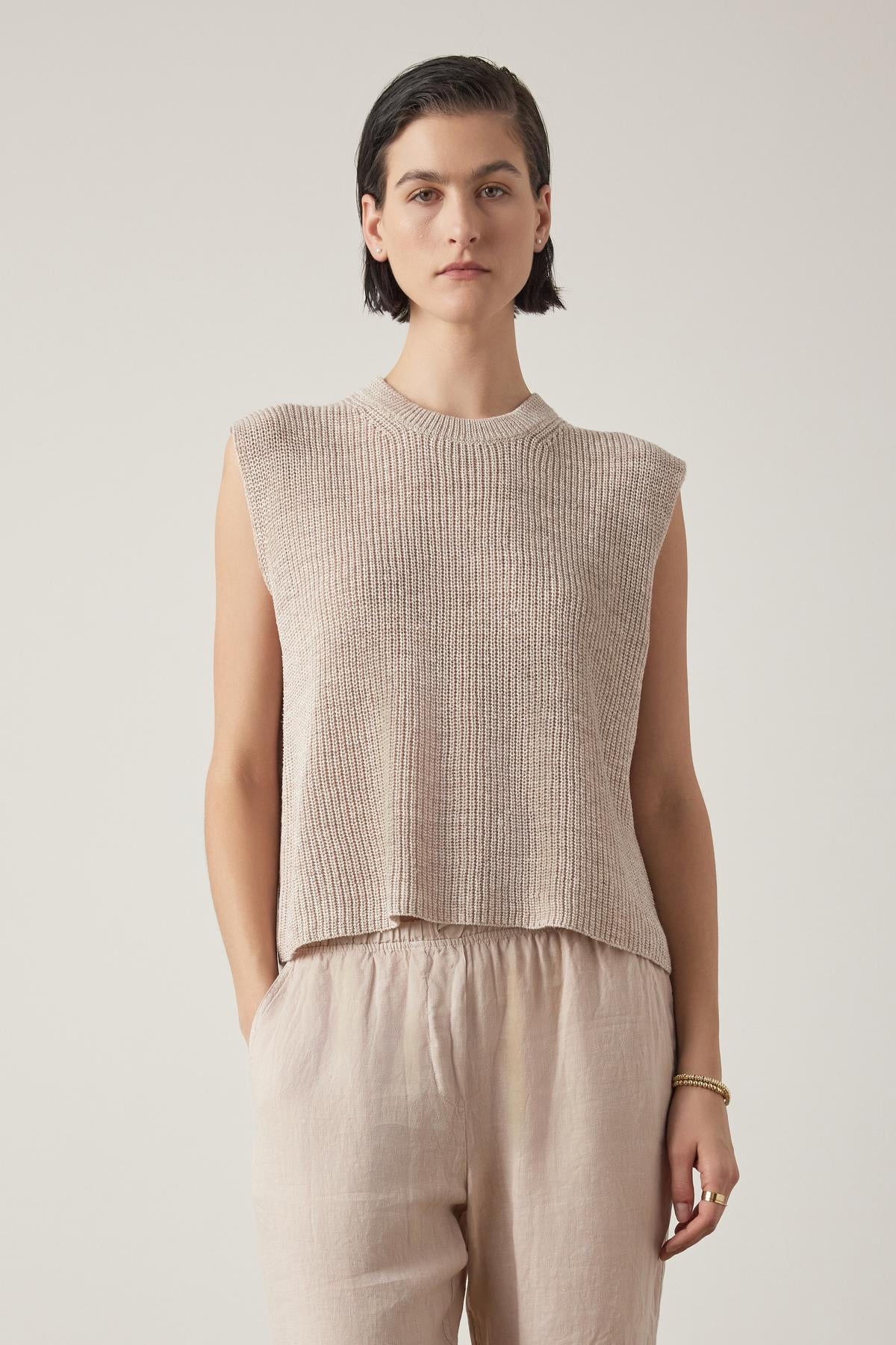   A person with short dark hair is wearing the Velvet by Jenny Graham's GARDENA LINEN SWEATER VEST and light brown relaxed fit pants, standing against a plain background. 