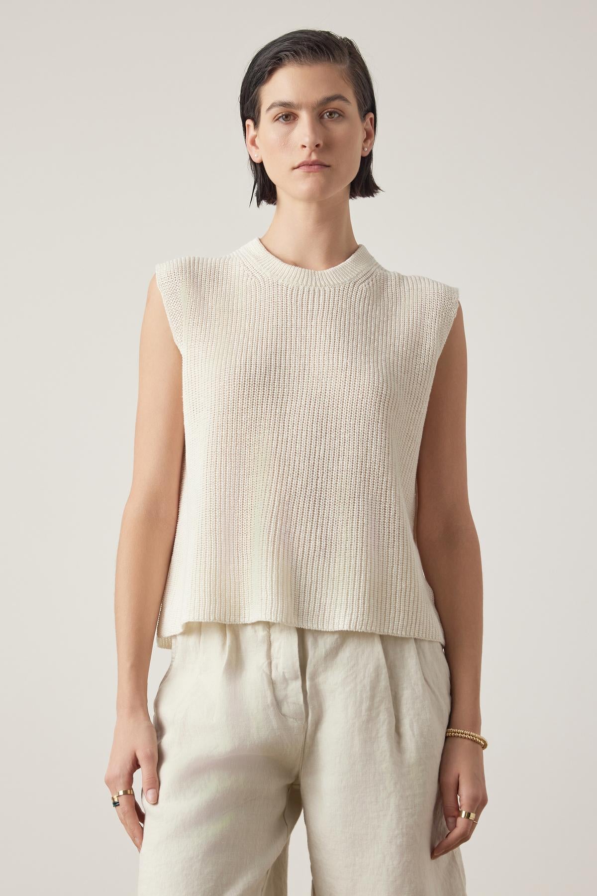   A person with short dark hair wearing the GARDENA LINEN SWEATER VEST by Velvet by Jenny Graham and relaxed fit, breathable linen pants stands against a plain background. 