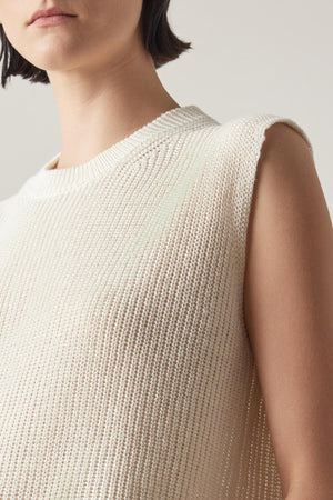 A person with short dark hair is wearing a sleeveless, breathable GARDENA LINEN SWEATER VEST in white by Velvet by Jenny Graham. The image focuses on the upper torso and lower face.