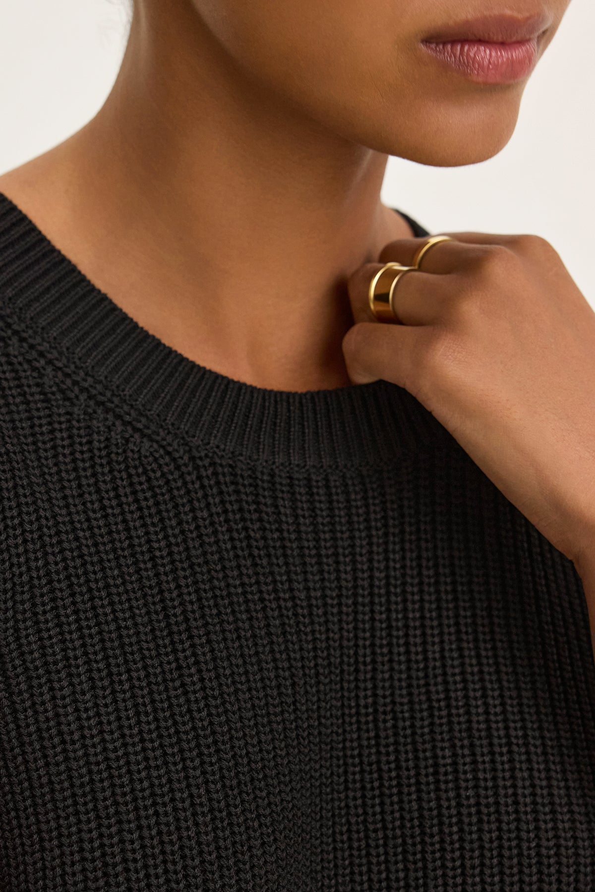 An individual wearing the MUNA SWEATER VEST by Velvet by Graham & Spencer enhances their layered style, with two gold rings on their fingers partially concealing their mouth.-38662690963649