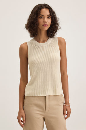 A person with curly hair wears a chic Velvet by Graham & Spencer MUNA SWEATER VEST in beige, crafted from textured cotton, paired with matching pants, against a plain background.