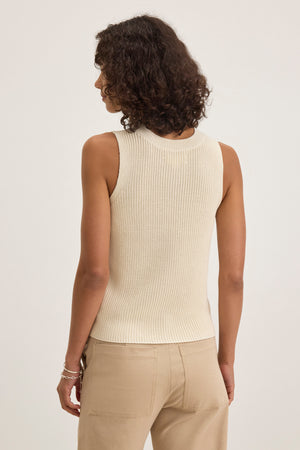 A person with curly hair wears the MUNA SWEATER VEST by Velvet by Graham & Spencer along with beige pants, viewed from behind against a plain backdrop.