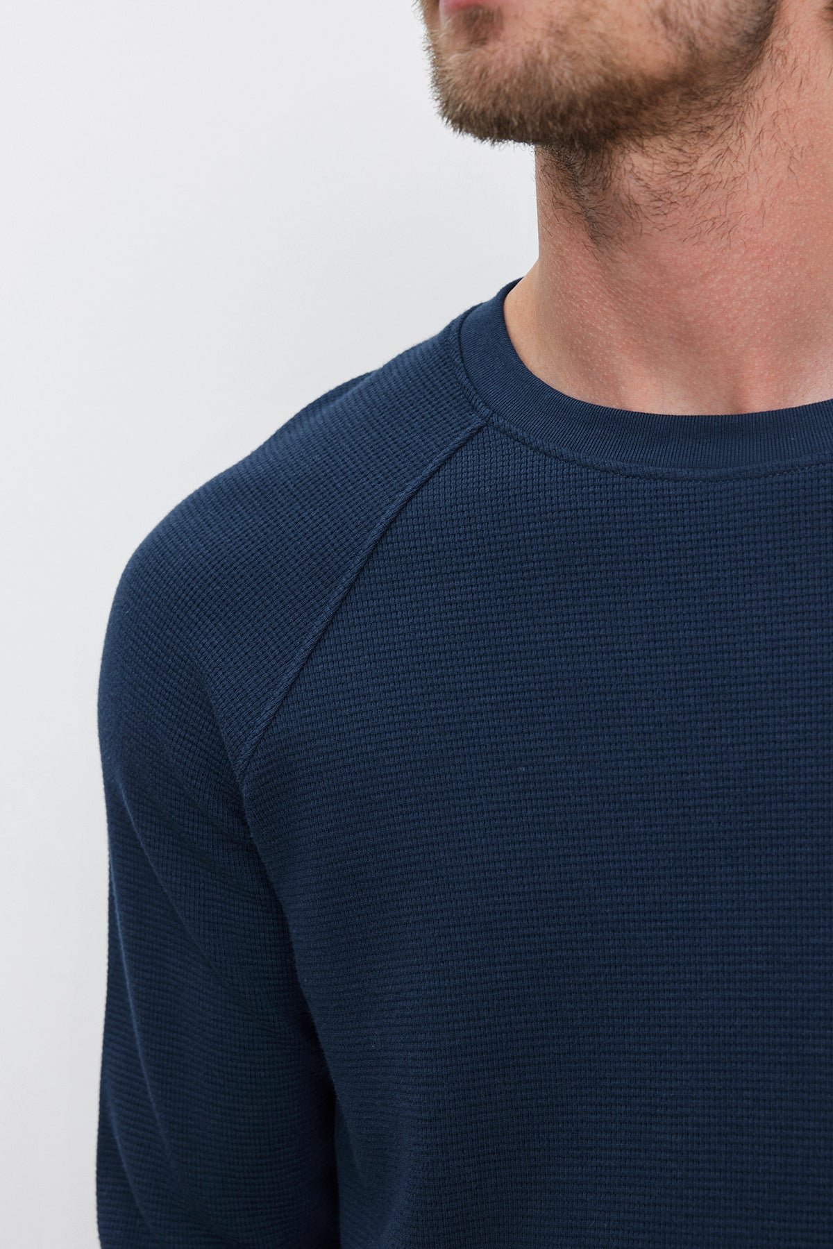 Close-up of a person wearing the GLEN THERMAL CREW, a dark blue textured long-sleeve shirt with a classic neckline by Velvet by Graham & Spencer. Their face is partially visible, focusing on the shoulder and neckline area.-37893764808897