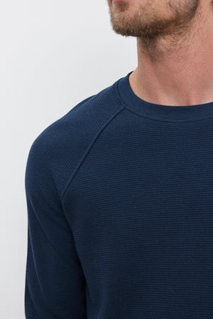 Close-up of a person wearing the GLEN THERMAL CREW, a dark blue textured long-sleeve shirt with a classic neckline by Velvet by Graham & Spencer. Their face is partially visible, focusing on the shoulder and neckline area.