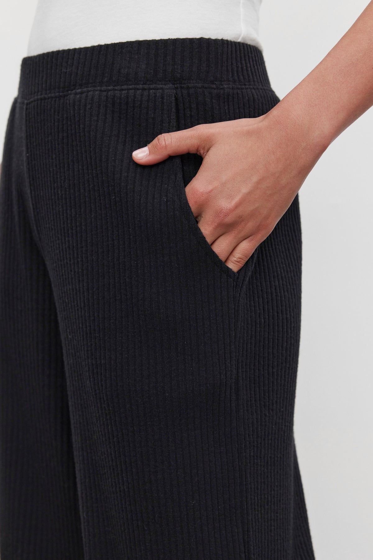   A person wearing the ultra-soft COLLEEN RIBBED PANT in black by Velvet by Graham & Spencer, with their right hand in the pocket, showcasing a stylish yet comfortable piece of everyday wear. 