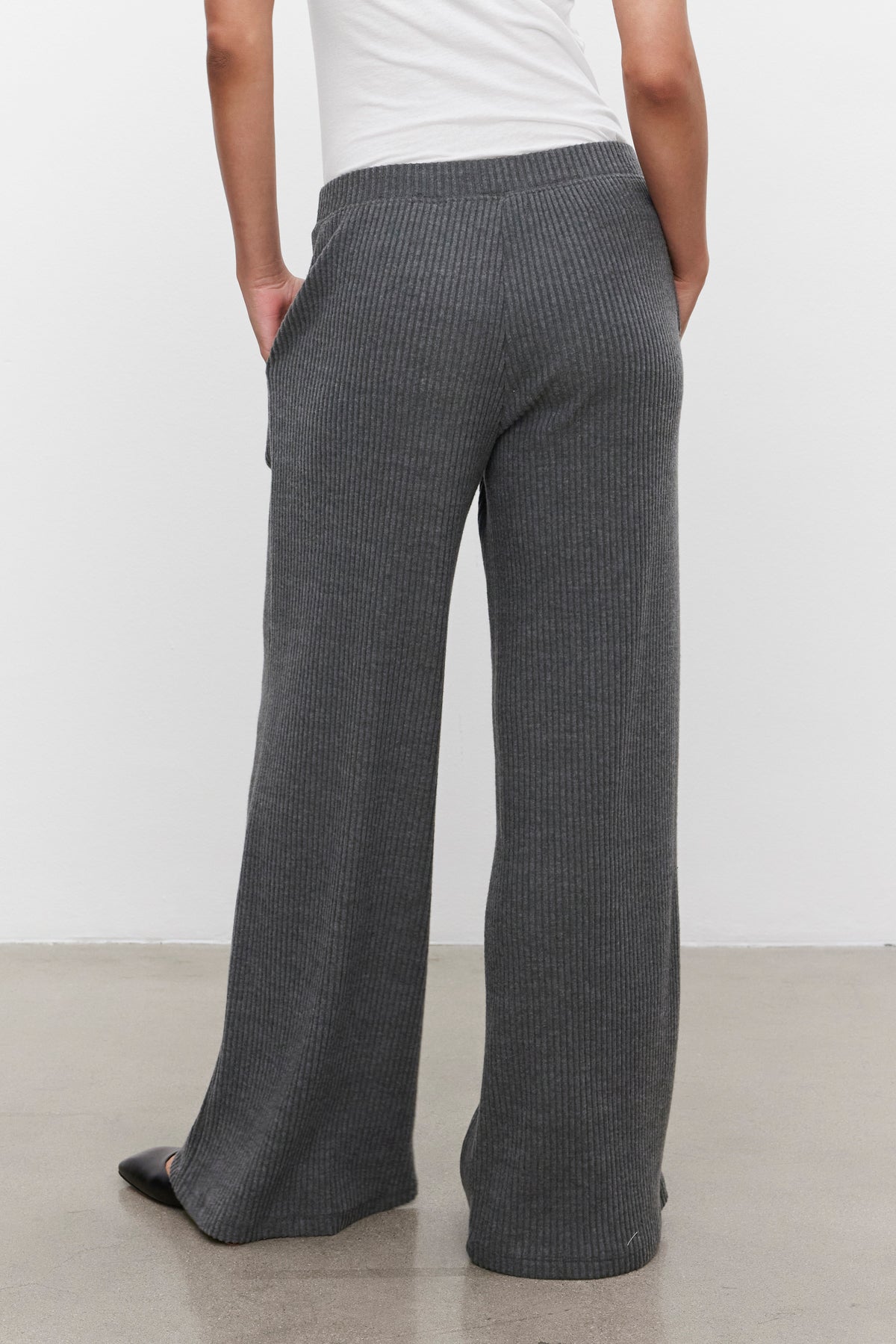   A person wearing Velvet by Graham & Spencer's COLLEEN RIBBED PANT in a loose-fitting, ultra-soft gray fabric stands with hands in pockets, facing away from the camera. 