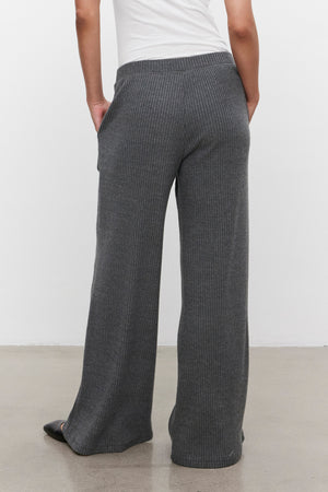 A person wearing Velvet by Graham & Spencer's COLLEEN RIBBED PANT in a loose-fitting, ultra-soft gray fabric stands with hands in pockets, facing away from the camera.