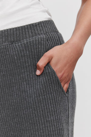 Close-up of a person wearing ultra-soft COLLEEN RIBBED PANT made from wide-leg, ribbed gray fabric by Velvet by Graham & Spencer, with their right hand placed in the pocket—perfect for everyday wear.