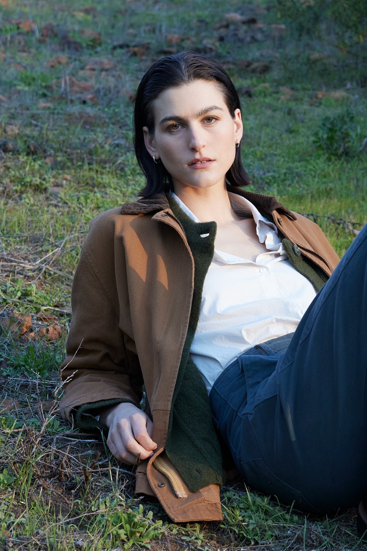 Person with short dark hair wearing the OAKLEY JACKET by Velvet by Jenny Graham, featuring corduroy trims, and a white shirt, lying on grass outdoors.-37676404179137