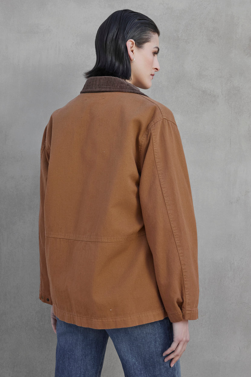 A person with short dark hair is seen facing away from the camera, wearing the OAKLEY JACKET by Velvet by Jenny Graham, which features corduroy trims, and pairing it with blue jeans while standing against a gray textured wall.