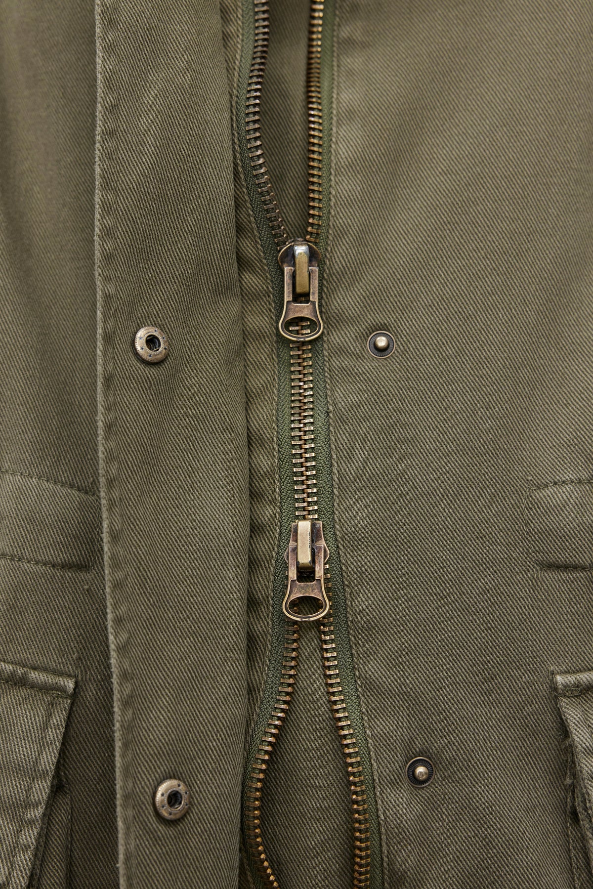   Close-up of the ODETTE JACKET by Velvet by Graham & Spencer in khaki green, featuring a classic collar, durable cotton twill fabric, and a double zipper front with snap buttons. The two zippers are partially unzipped, revealing the overlapping fabric detail. 