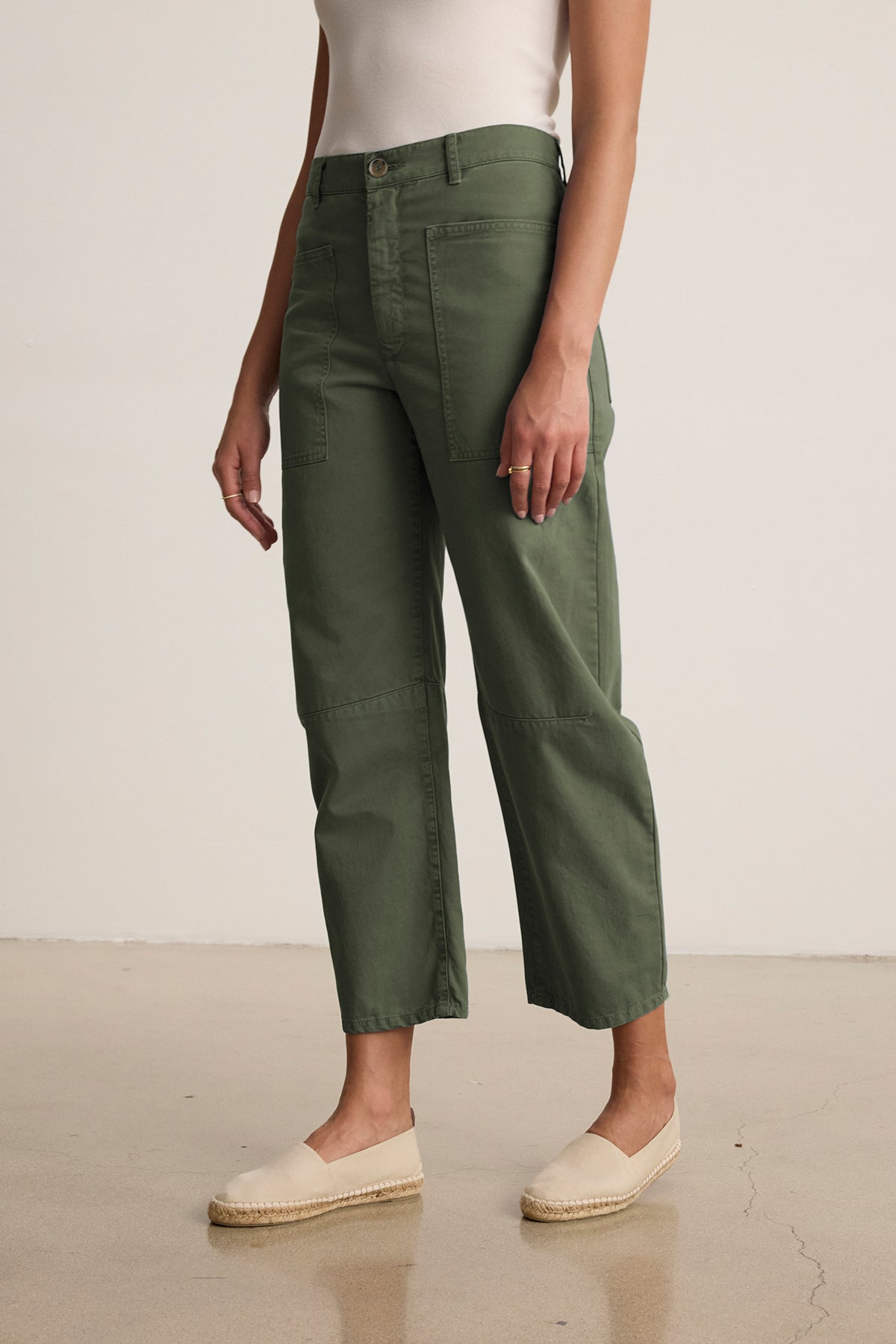 Someone stands on a polished floor wearing Velvet by Graham & Spencer's BRYLIE SANDED TWILL UTILITY PANT in green, paired with a white sleeveless top and beige espadrilles.-38807322689729