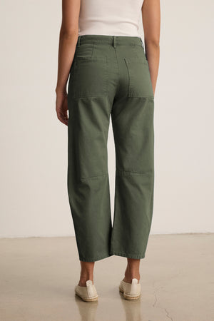 A person wearing a white top and the BRYLIE SANDED TWILL UTILITY PANT by Velvet by Graham & Spencer, featuring green wide legs and patch pockets, stands on a plain floor, facing away.