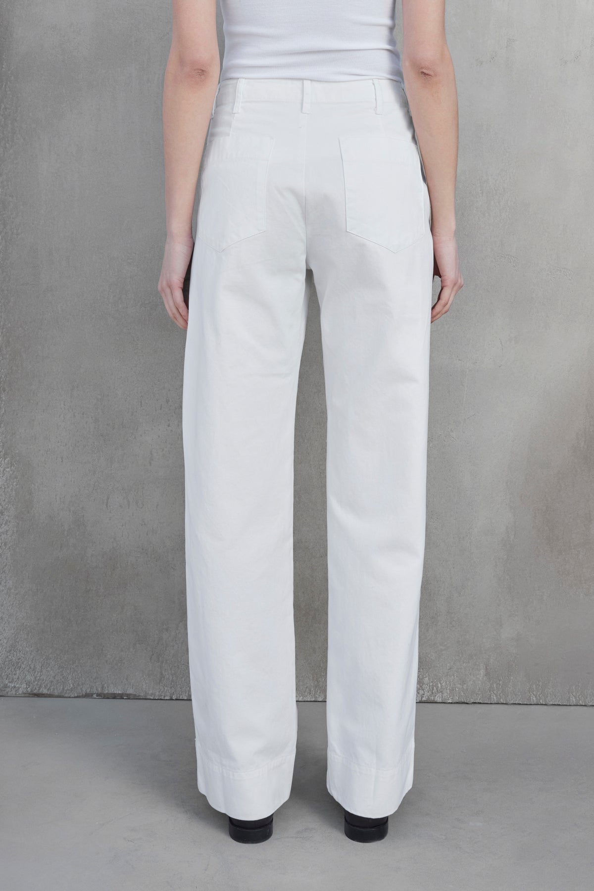   Rear view of a person wearing the VENTURA PANT — white high-waisted, wide-leg pants made from cotton twill by Velvet by Jenny Graham — paired with a matching top, standing against a neutral gray background. 