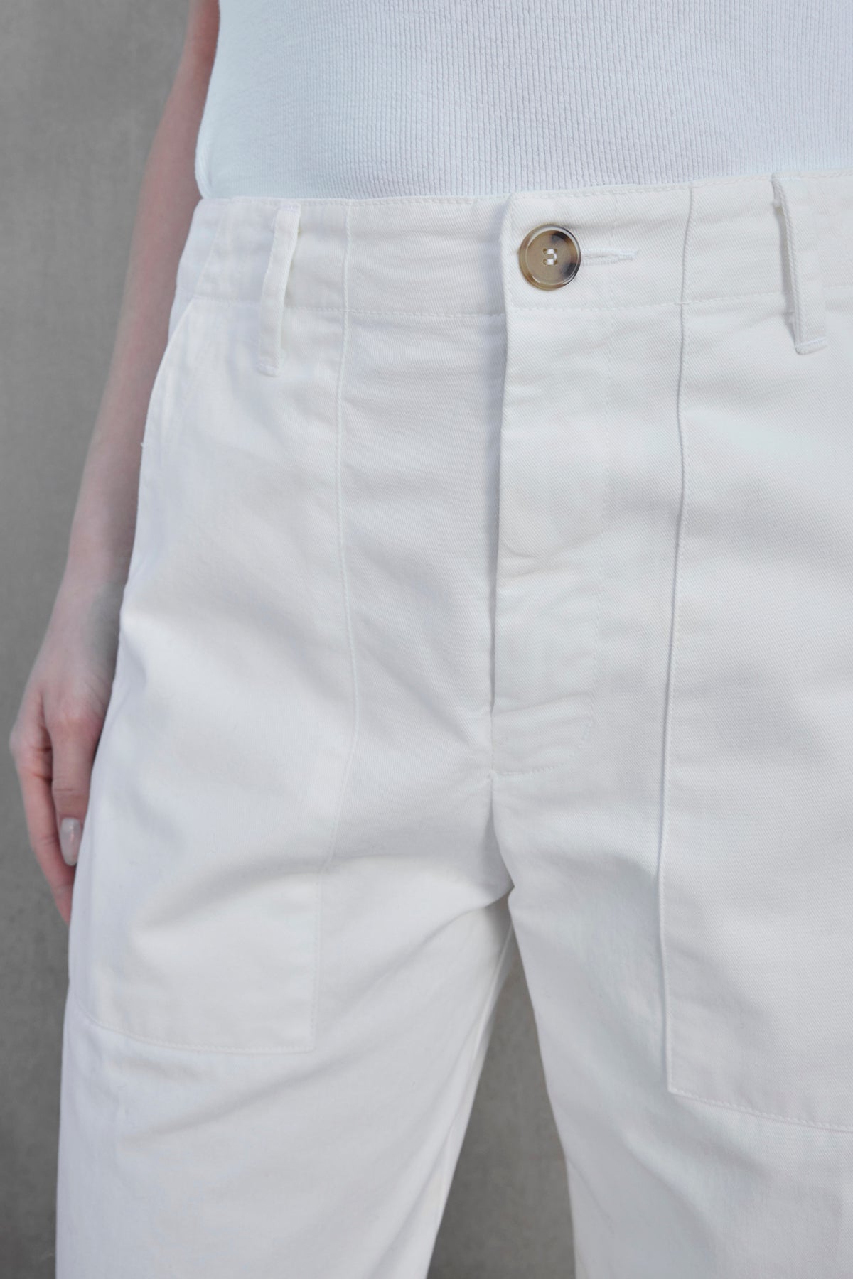   Close-up view of a person wearing the VENTURA PANT by Velvet by Jenny Graham, featuring white, high-waisted wide-leg pants with a single button closure and a tucked-in white top. The outfit exudes a subtle utilitarian vibe, perfect for both casual and chic occasions. 