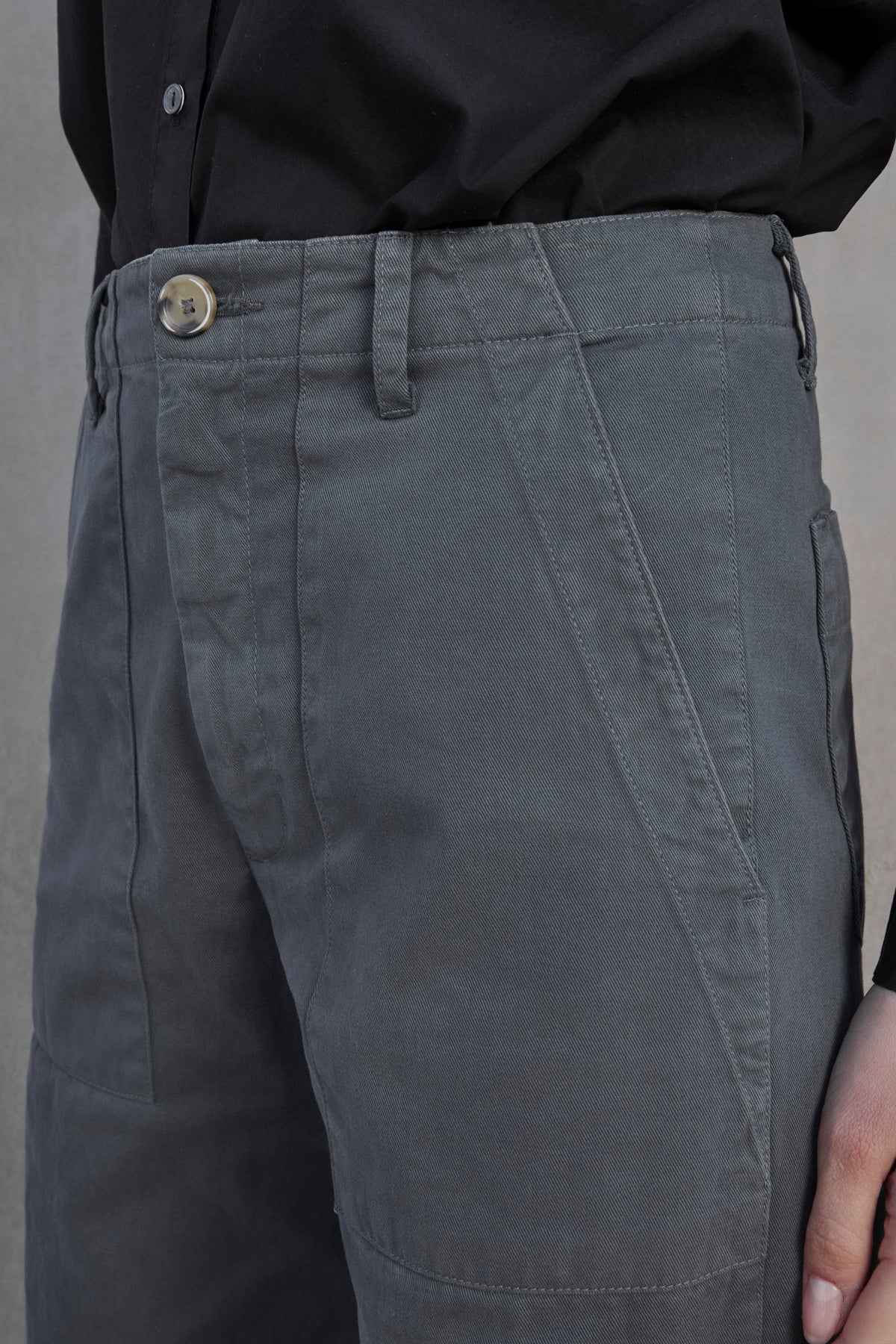 Close-up of a person wearing VENTURA PANT from Velvet by Jenny Graham, featuring grey, cotton twill fabric with a buttoned waist and front pockets, paired with a black shirt.-37659921973441