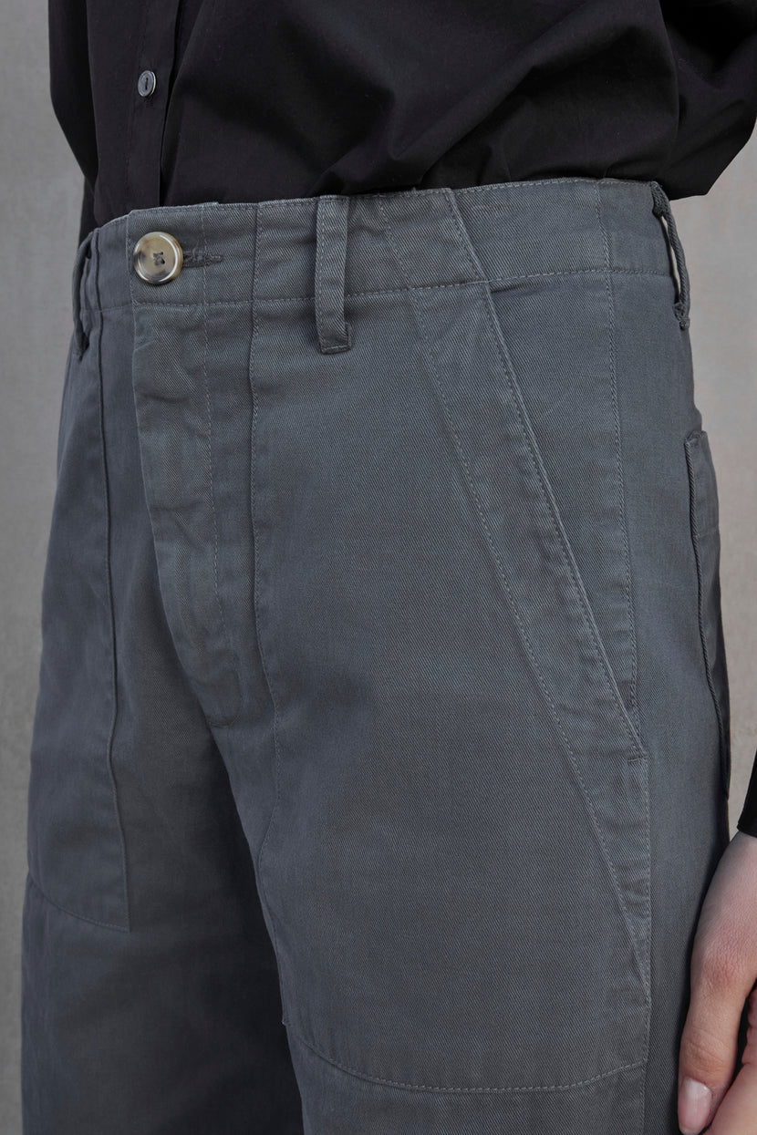 Close-up of a person wearing VENTURA PANT from Velvet by Jenny Graham, featuring grey, cotton twill fabric with a buttoned waist and front pockets, paired with a black shirt.