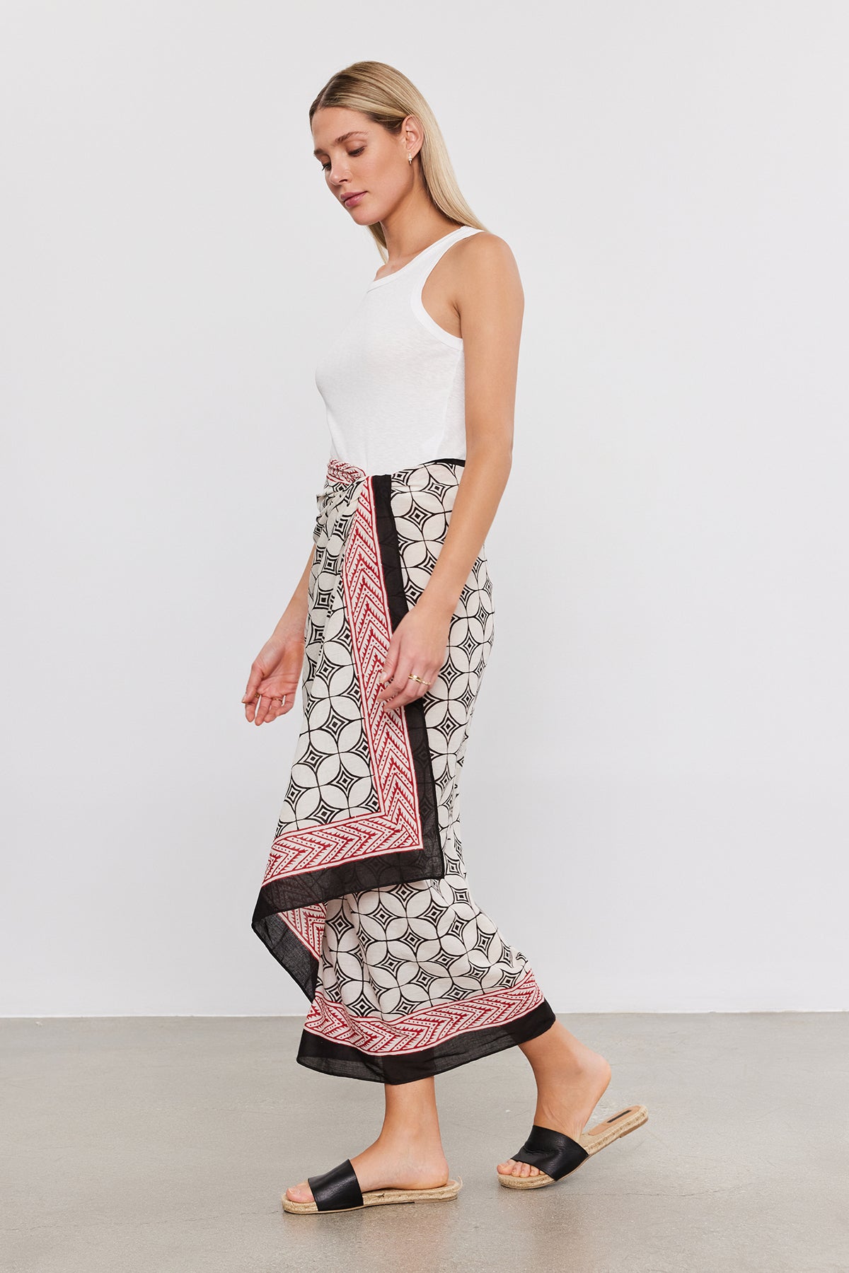 A person wearing a white sleeveless top, Velvet by Graham & Spencer SARONG WRAP, and black sandals stands against a plain white background.-37367009542337