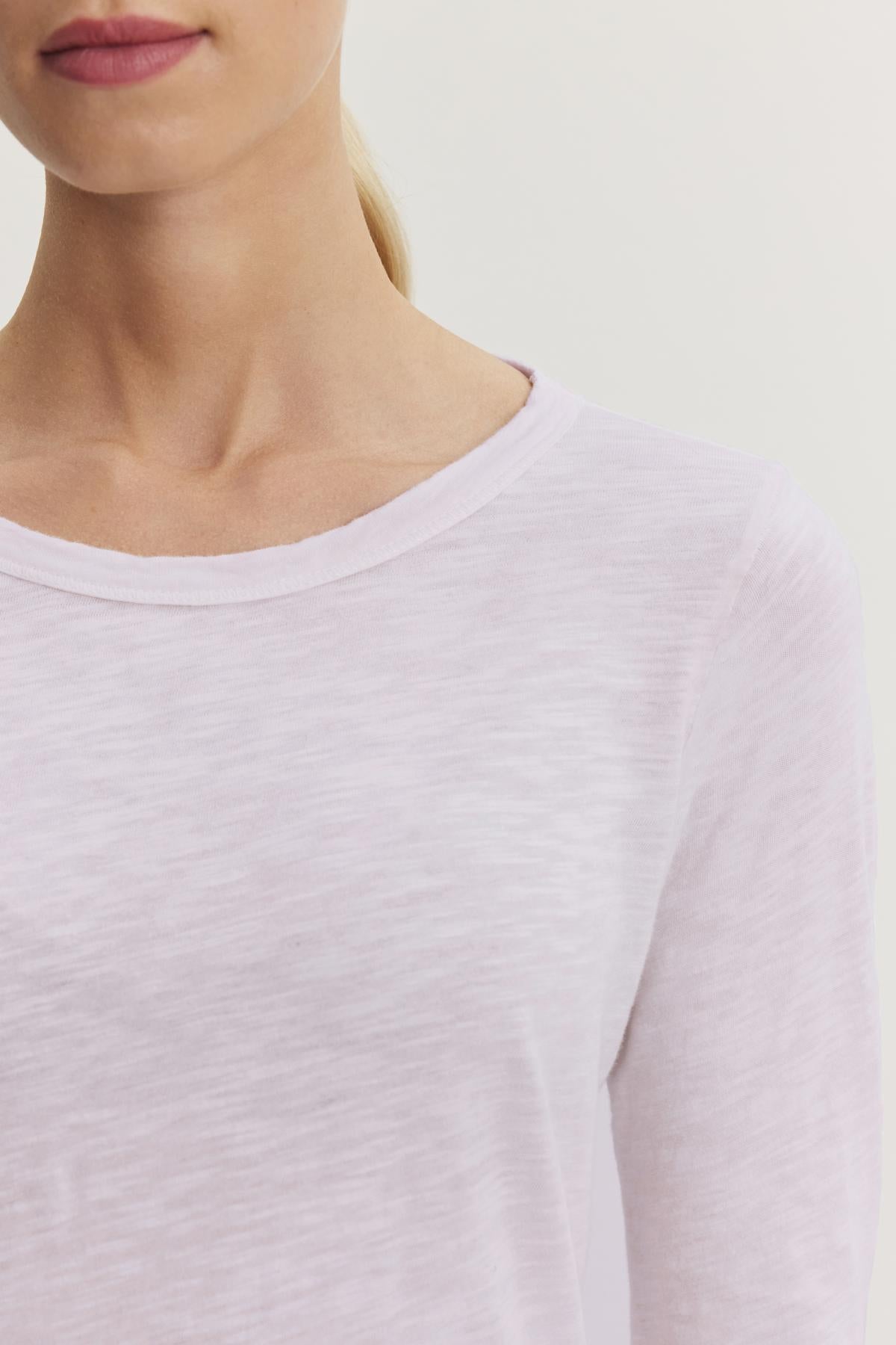   The individual is dressed in the Velvet by Graham & Spencer's LIZZIE TEE, a textured cotton slub long-sleeve shirt in light pink, pictured from shoulders to upper chest with minimal background detail. 