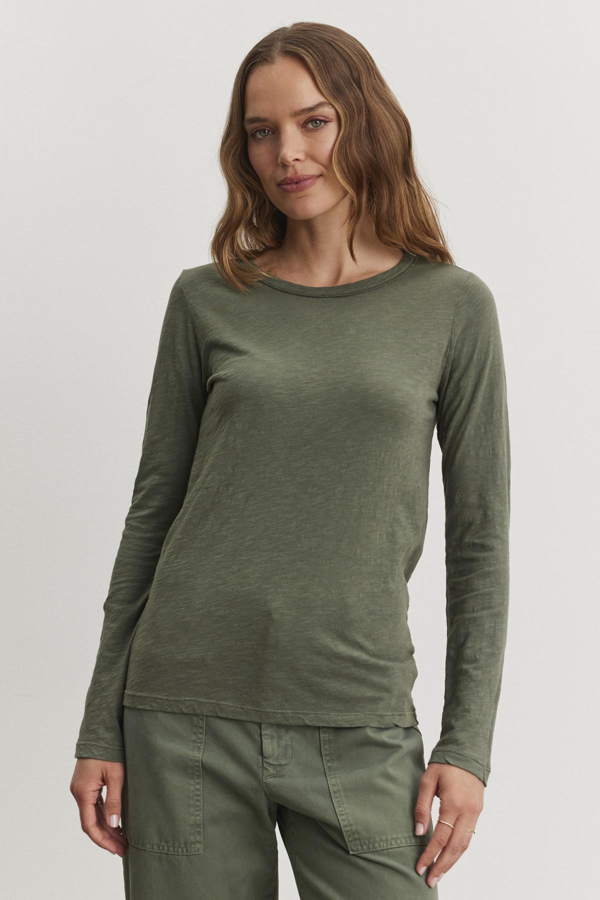   A person with long hair wears a LIZZIE TEE by Velvet by Graham & Spencer in green, complete with long sleeves and matching pants, standing against a plain background. 